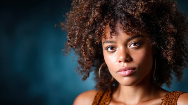A stunning portrait showcasing a young woman's beautiful curly hair and engaging expression against a soft, blurred background with a dramatic tone.
