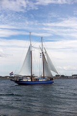 Traditional blue two-masted schooner with white sails catching the wind on sea water with soft cloudy blue sky during Hanse Sail festival. © Olena