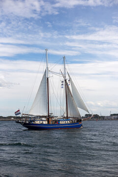 Traditional blue two-masted schooner with white sails catching the wind on sea water with soft cloudy blue sky during Hanse Sail festival.