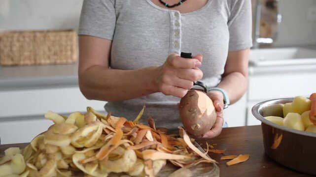 Girl Peeling Raw Sweet Potatoes For Dinner With Potato Peeler in Kitchen