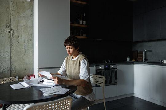 Worried woman checking financial documents at desk at home kitchen