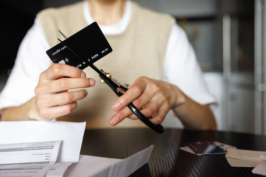 Cropped view of woman cutting credit card with scissors at desk