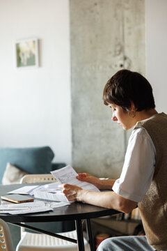 Serious woman checking financial documents at desk at blurred home