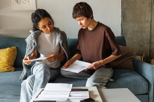 Young focused multiethnic women checking financial documents on sofa
