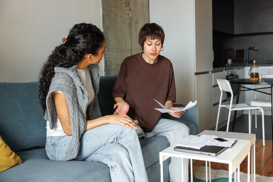 Woman looking at worried girlfriend with financial documents in hand