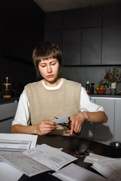 Young serious woman cutting credit card with scissors at desk at home