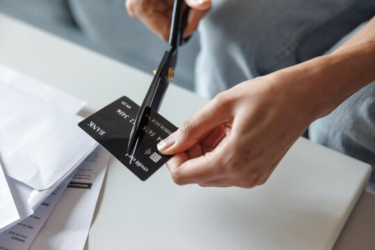 Cropped of woman cutting credit card with scissors at table on couch