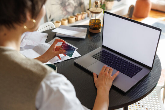 Cropped woman paying with credit card on laptop at desk at home