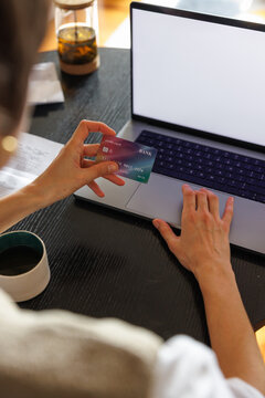 Cropped woman paying with credit card on laptop at desk at home
