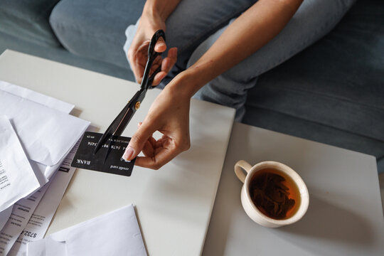 Partial of woman cutting credit card with scissors at desk on sofa