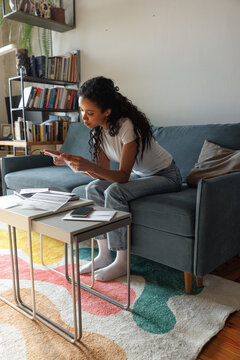 Young black focused woman reading financial documents at desk on sofa