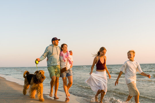 Family Walking Along Beach With Dog at Sunset 