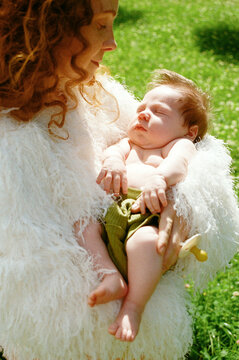 A mother holds her baby in her arms on a sunny day.