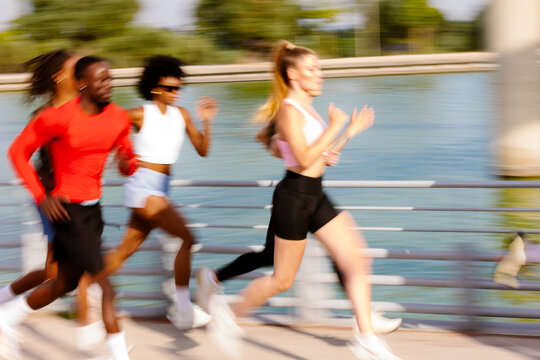 Motion-blurred shot of diverse running group jogging past a calm lake