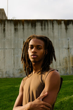 Young man with dreadlocks, serious expression, arms crossed in park