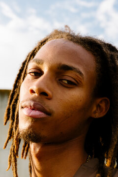 Confident young Black man with dreadlocks, serious headshot in park