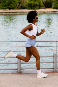 Black female athlete sprinting along a lake on a sunny morning