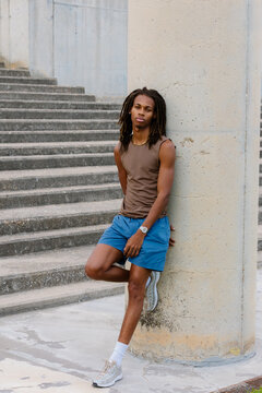 Full-body portrait of a fit Black man leaning against a park pillar