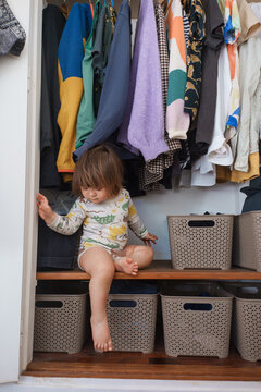 Child Sitting in Closet Among Clothes and Storage Boxes