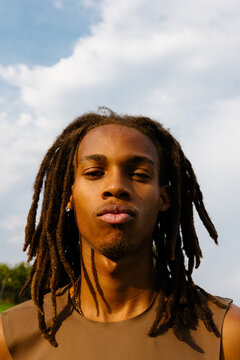 Serious young Black man with dreadlocks, sunlit outdoor headshot