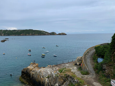 A high-angle, eye-level shot overlooking the picturesque Saints Bay in the parish of St. Martin, Guernsey. The image captures a cluster of small fishing boats and tenders bobbing peacefully
