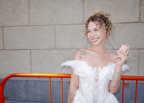 Bride in white dress holding vape against urban wall