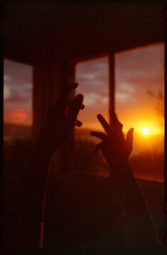 Silhouette of raised hands against a vivid ocean sunset on film