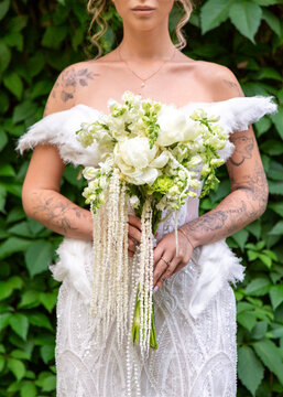 Tattooed bride holding white and green wedding bouquet outdoors