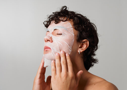 Person Applying a Sheet Mask to Their Face Indoors in a Simple Setting