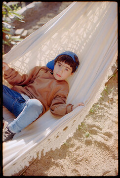 Little boy in blue cap relaxing on a white hammock on 35mm film