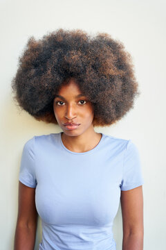 Woman With Big Curly Hair Stands in Front of a Plain Wall