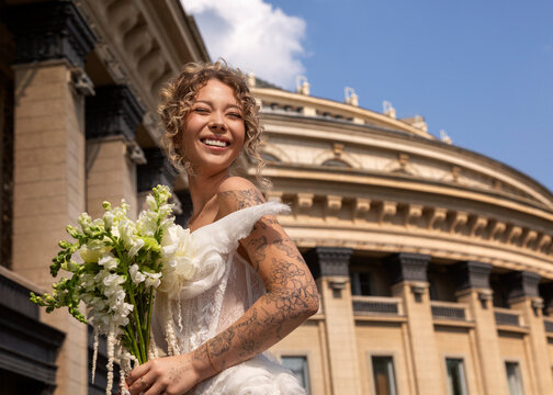 Bride holding bouquet smiling in front of historic building