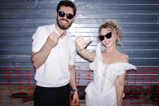 Bride and groom wearing sunglasses posing against blue wall