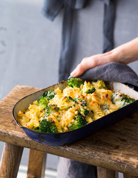 Hand holds a casserole with macaroni and broccoli