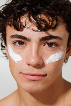 Young Man Applies Skin Cream on His Face in a Bright Setting