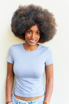 Smiling Woman With Large Curly Hair Standing Against a Wall
