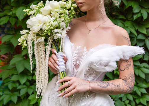 Tattooed bride holding white flower bouquet outdoors