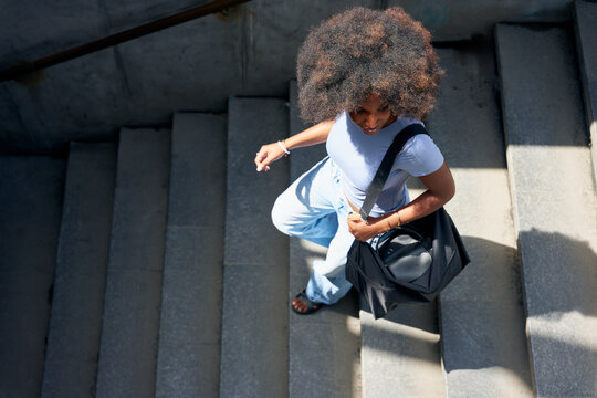 Individual Walks Down Stairs in an Urban Area With a Bag
