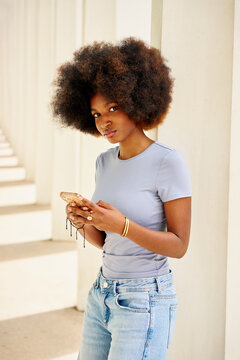 Young Person Holds Smartphone and Stands Near White Pillars