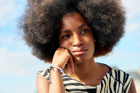 Woman Relaxes Outdoors With Thoughtful Expression in Daytime Sky