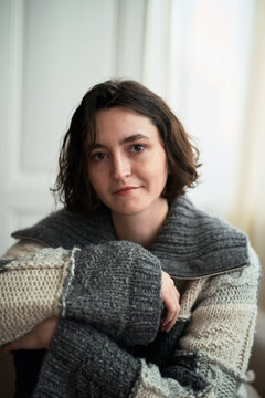 Woman in Cozy Sweater Sitting Indoors and Looking at Camera