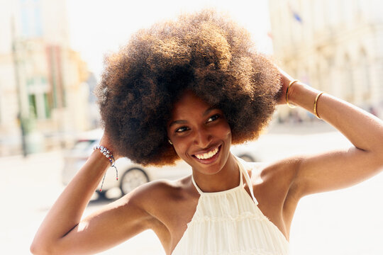 Woman Smiles While Touching Her Hair in a Sunny Outdoor Location