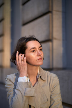 Woman Touches Her Hair While Standing Near a Building in the Evening