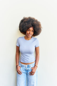 Woman Stands Against Light Wall With Relaxed Pose in Casual Outfit