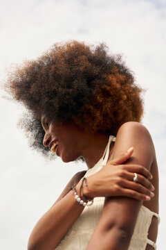 Woman With Curly Hair Smiles Outdoors Under Cloudy Sky