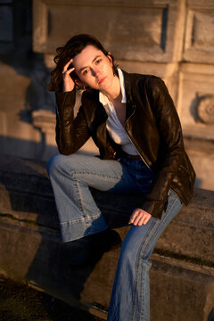 Young Woman Sits on a Stone Wall in a City During Sunset
