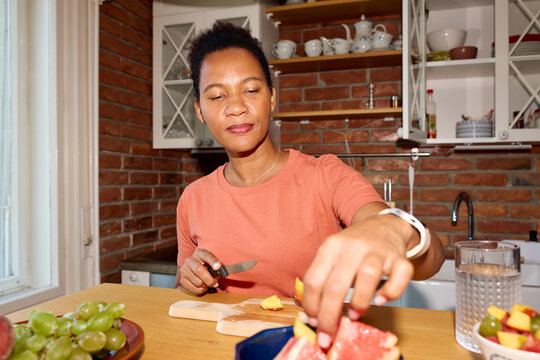 Pleased woman prepares fruit salad at home