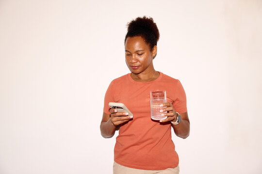 Woman holds a glass of water while checks her phone