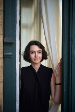 Young Woman Standing by a Window Holding a Curtain