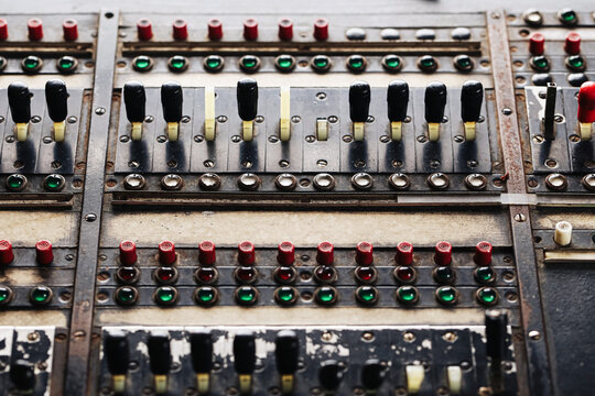 Vintage industrial control panel with rows of black levers red switches and green indicator lights. Aged electrical machinery console engineering equipment factory controls and technology background.